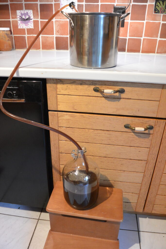 The pan sits on the counter. The carboy is on a stool on the floor. The siphon goes from the pan to the jug.